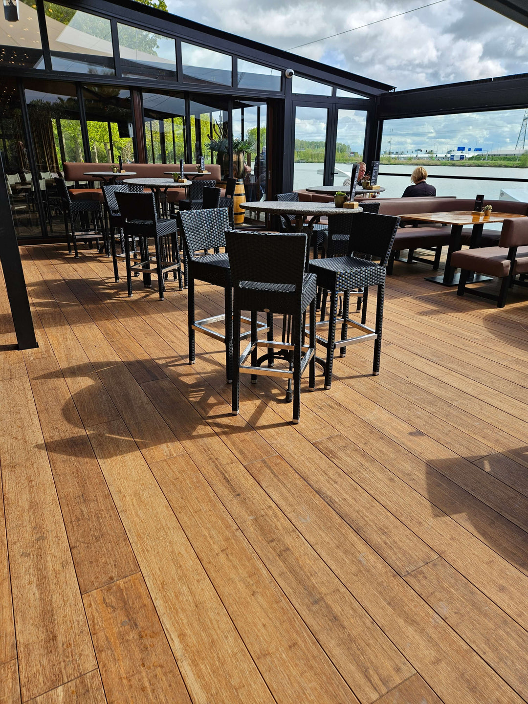 Widerstandsfähige Terrassendiele in Sand  färbend von aMbooo aus Bambus  verlegt in einer  Gastronomie mit Blick aufs Wasser.