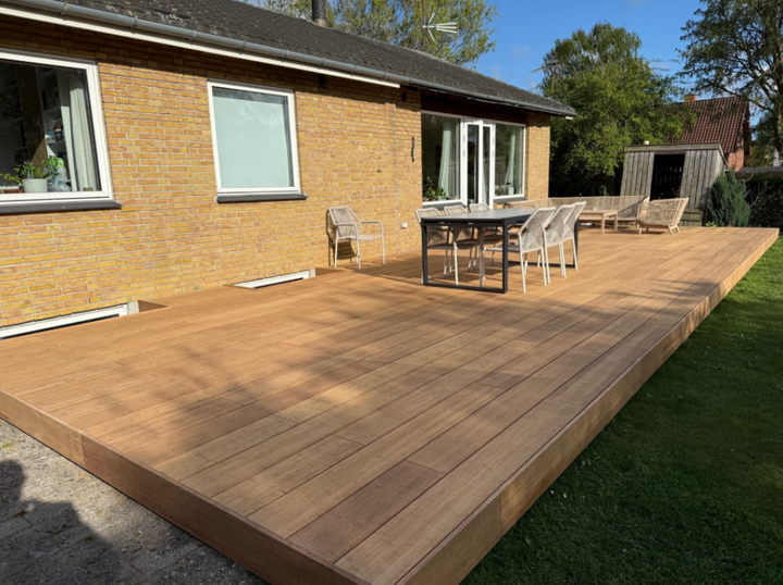 Großzügige Terrasse aus Closeddecking aMboooBambus Terrassendielen in natürlicher Holzoptik, ausgestattet mit modernem Essbereich und Lounge-Möbeln, vor einem Einfamilienhaus mit gelber Klinkerfassade – pflegeleicht und wetterbeständig