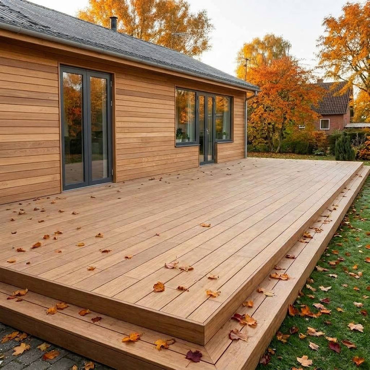 Große Holzterrasse an einem  Wohnhaus mit einer Holzfassade, umgeben von herbstlich gefärbten Bäumen und verstreutem Laub.