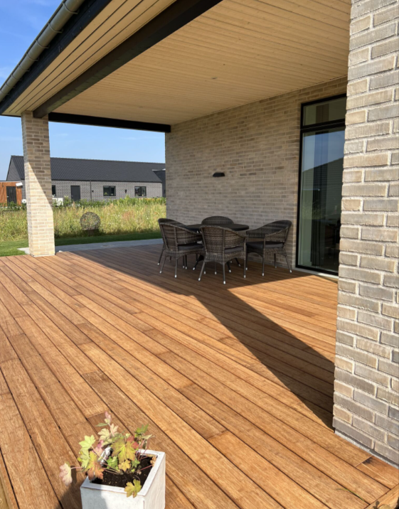 Weitläufige Terrasse aus Bambusdielen neben einem Haus mit Sitzgruppe und Blick in einen gepflegten Garten.