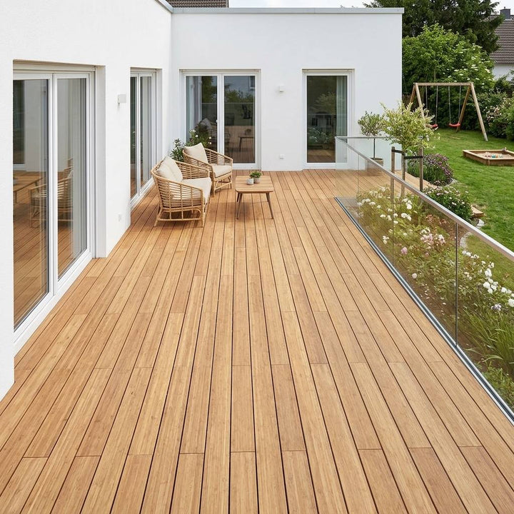 Großzügige Bambusholzterrasse mit zwei Sesseln, Glastisch und Glasgeländer vor einem weißen Wohnhaus mit Blick in den Garten.
