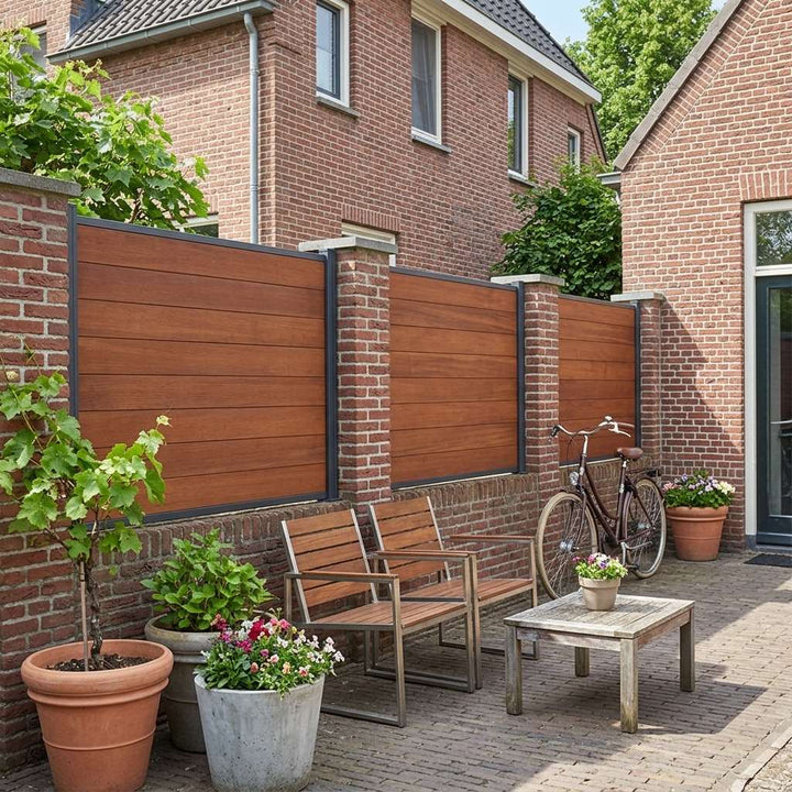 Gepflasterter Innenhof mit Holzstühlen, kleinem Tisch, Blumenkübeln und Fahrrad vor einem Sichtschutzzaun in Holzoptik mit Backsteinpfeilern.
