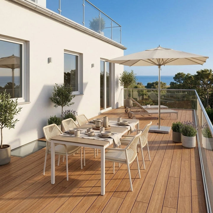 Überdachte Holzterrasse mit Essplatz, Loungemöbeln, Glasgeländer und Meerblick vor einem weißen Wohnhaus.