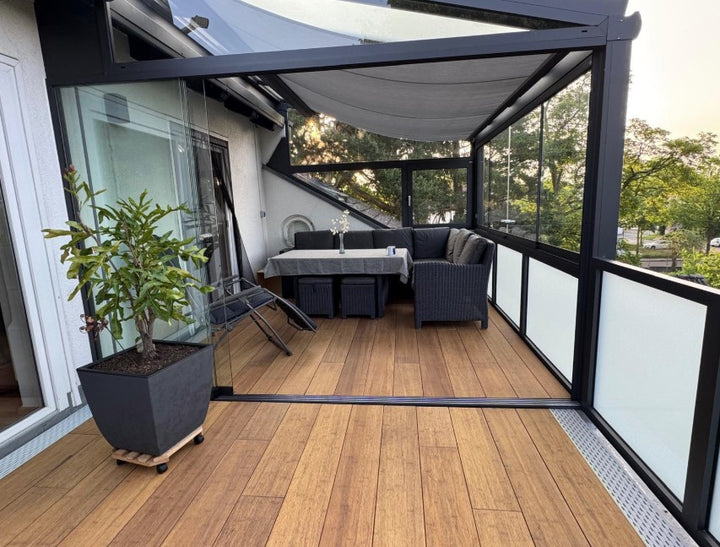 Die aMBOOO Closed Decking Bambusdiele Cristobal  unter moderner Überdachung an einem Einfamilienhaus, ausgestattet mit Gartenmöbeln. Nachhaltige Bambusdielen mit natürlicher Holzoptik, ideal für stilvolle und wetterfeste Terrassengestaltung.