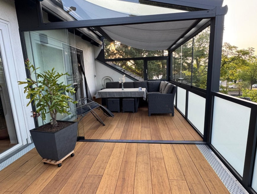 Die aMBOOO Closed Decking Bambusdiele Cristobal  unter moderner Überdachung an einem Einfamilienhaus, ausgestattet mit Gartenmöbeln. Nachhaltige Bambusdielen mit natürlicher Holzoptik, ideal für stilvolle und wetterfeste Terrassengestaltung.