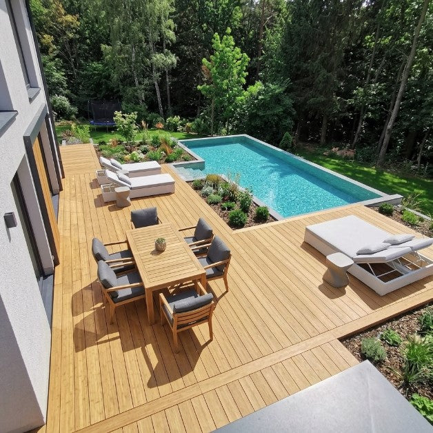 Moderne Poolterrasse aus Colon Closeddecking Terrassendielen mit Essbereich, Sonnenliegen und Blick auf den Garten.