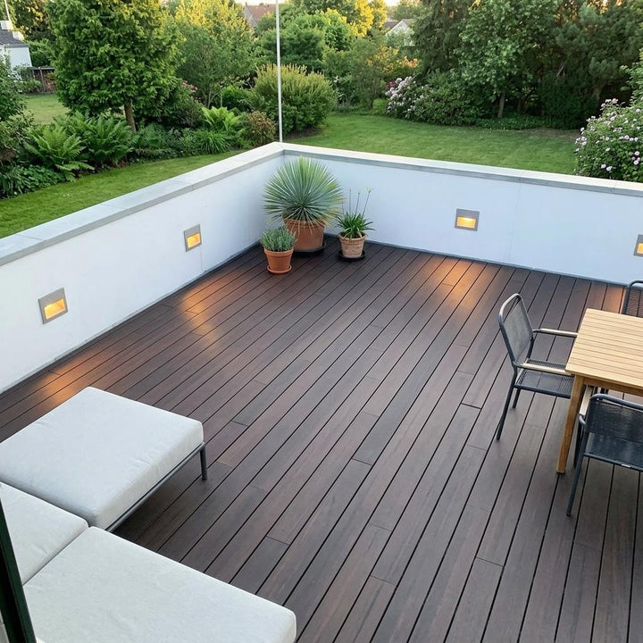 Großzügige Dachterrasse mit dunkelbraunen AMBOOO-Terrassendielen, Sitzmöbeln, Pflanzkübeln und Blick in einen grünen Garten.