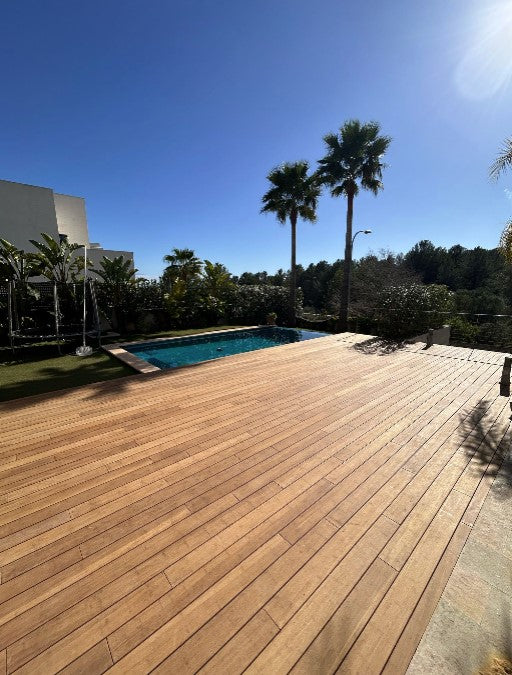 Große Terrasse mit Bambus-Terrassendielen in Holzoptik Farbe Sand, neben einem Swimmingpool und Palmen unter blauem Himmel.