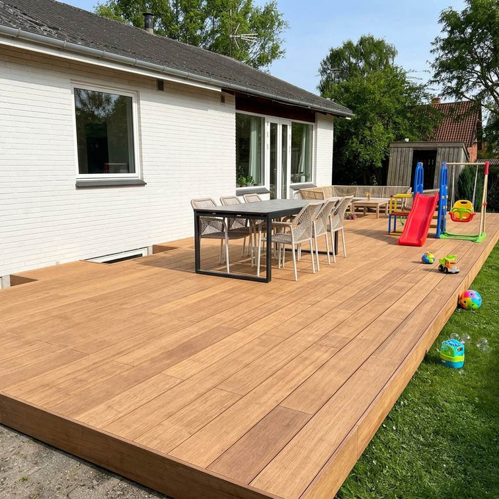Große Holzterrasse mit Esstisch, Sitzgruppe, Rutsche, Schaukel und Kinderspielzeug vor einem weißen Wohnhaus.