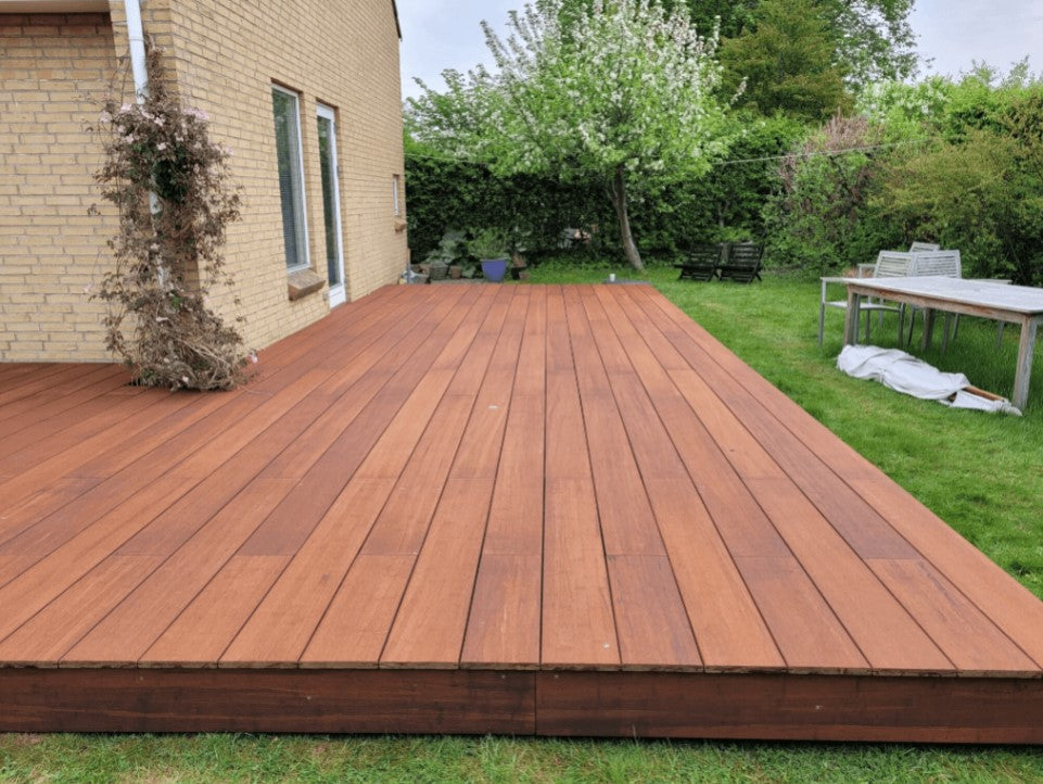 Moderne Terrasse mit XL Terrassendielen aus Bambusholz an einem Einfamilienhaus, hochwertig verlegt in geradlinigem Muster auf grüner Rasenfläche.
