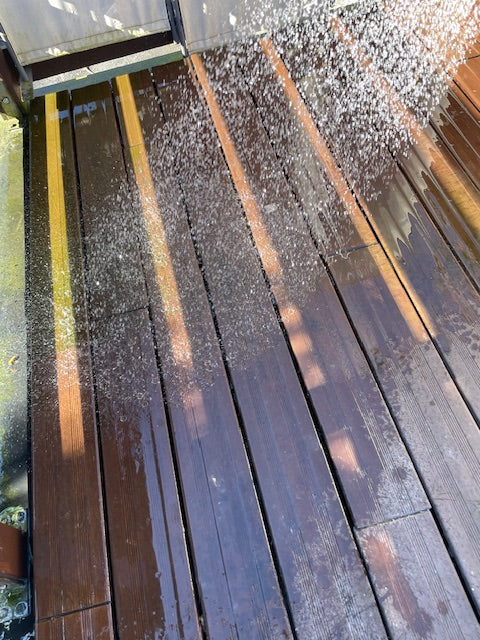 Wasser spült eine dunkelbraunes Bambusholz während der Reinigung ab. Die Terrassendielen werden nach dem Bürsten von Schmutz und Ablagerungen befreit.