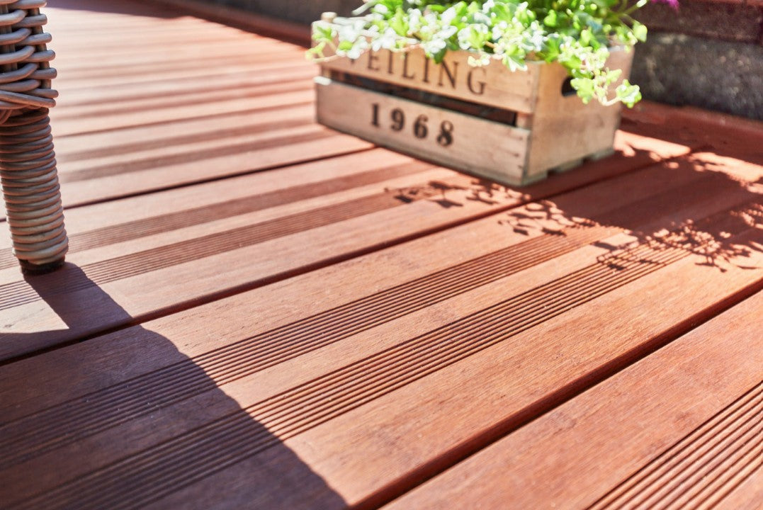 Detailaufnahme einer hochwertigen Bambus-Terrasse mit geriffelter Oberfläche, dekorativer Pflanzkiste und Gartenmöbeln im Sonnenlicht.
