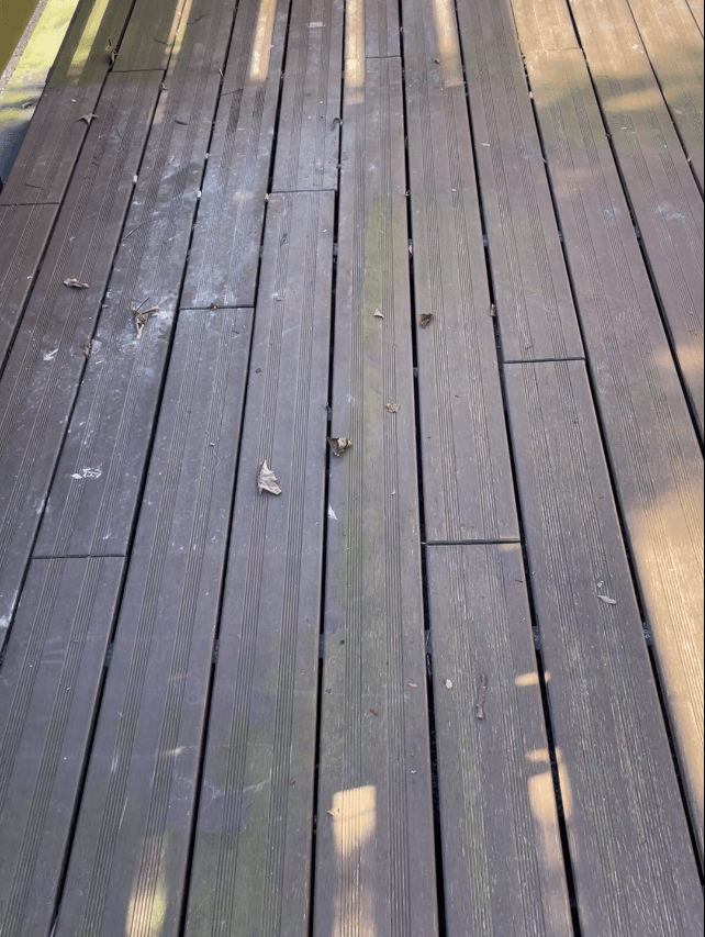 Verwitterte Terrasse mit dunkelbraunen Terrassendielen, die durch Witterungseinflüsse und Verschmutzungen ungleichmäßig gealtert sind.