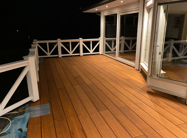 Moderner Balkon mit glatten Bambus-Terrassendielen und weißem Geländer bei stimmungsvoller Abendbeleuchtung.