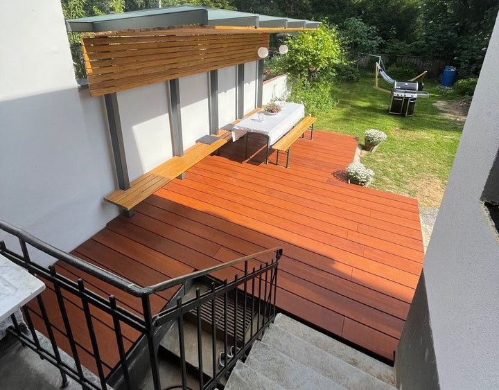 Moderne Holzterrasse mit überdachtem Sitzbereich, Esstisch, integrierten Sitzbänken und angrenzendem Garten mit Grill und Hängematte.