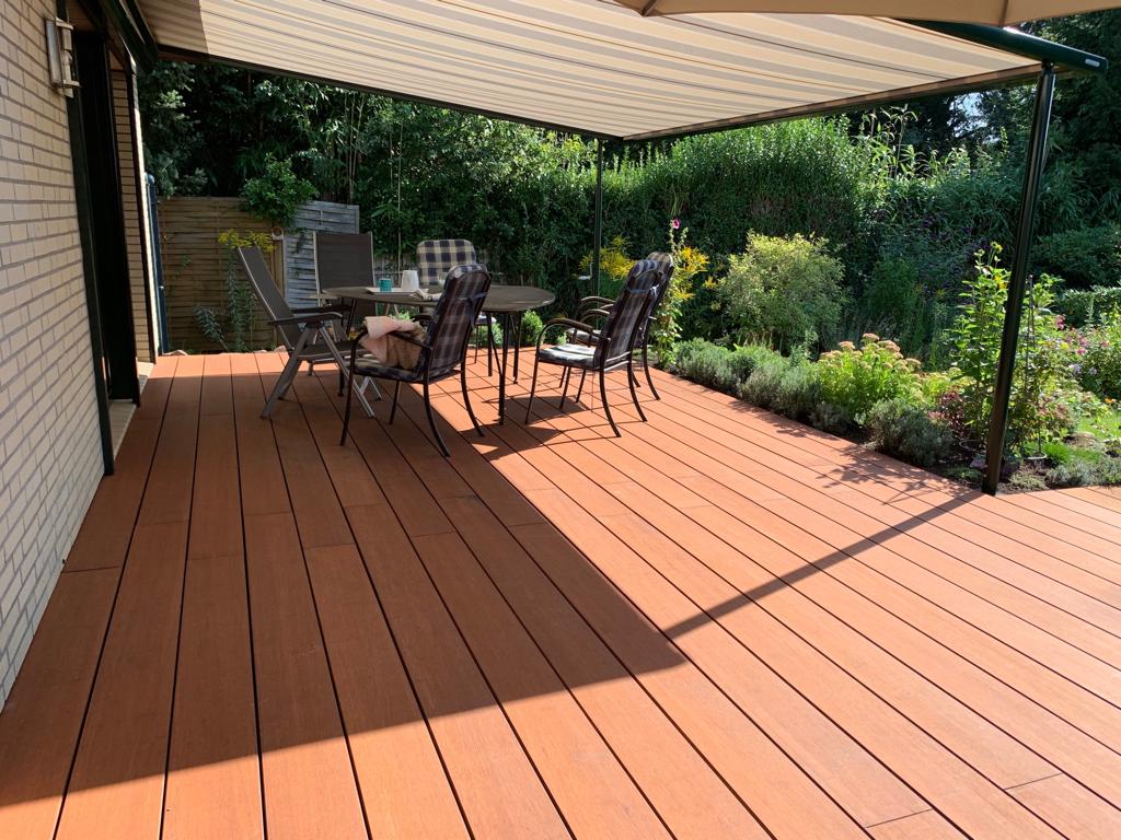 Moderne Terrasse mit Markise, Sitzgruppe und Blick auf einen liebevoll angelegten Garten an einem sonnigen Tag