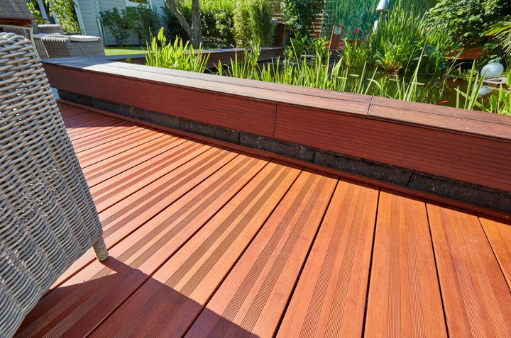 Moderne Holzterrasse mit rutschhemmenden Terrassendielen, eingefasstem Hochbeet und idyllischem Gartenteich im Hintergrund.