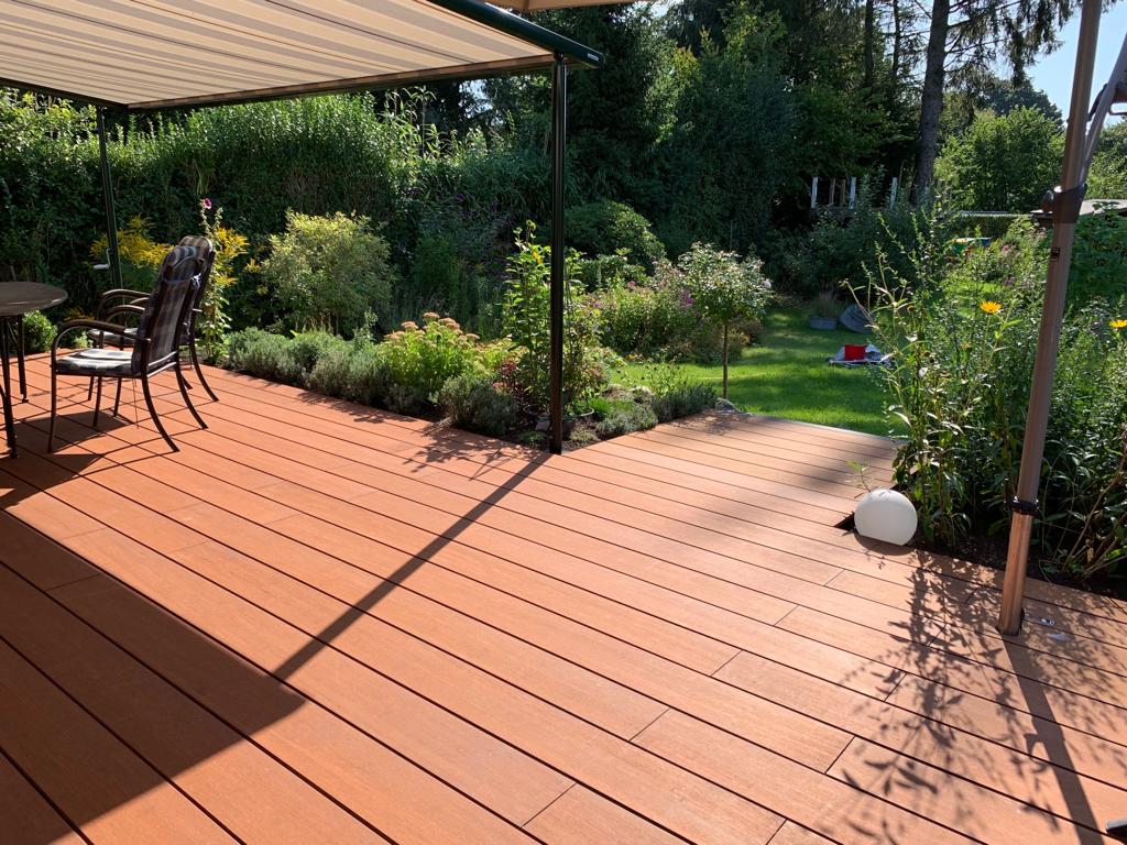 Moderne Terrasse mit Markise, Sitzgruppe und Blick auf einen liebevoll angelegten Garten an einem sonnigen Tag.