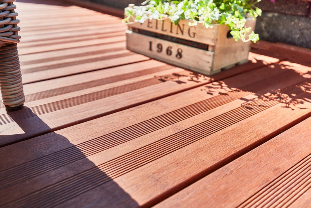 Detailaufnahme einer hochwertigen Bambus-Terrasse mit geriffelter Oberfläche, dekorativer Pflanzkiste und Gartenmöbeln im Sonnenlicht.